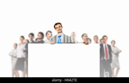 Image of young man holding blank banner with crowd of business people at background Stock Photo