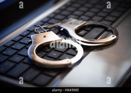 Selective focus on handcuffs on a keyboard cyber crime, hacking, bullying Against law concept in dark low key tone Stock Photo