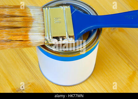 A flat brush on a paint can on a wooden panel. Stock Photo