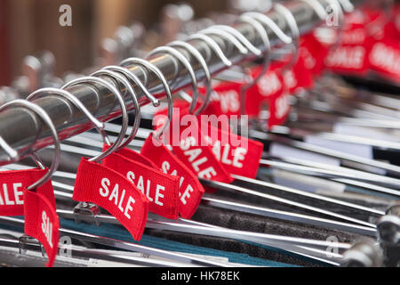 red labels with the word sale on clothes hangers outside fashion store Stock Photo