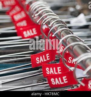 red labels with the word sale on clothes hangers outside fashion store Stock Photo