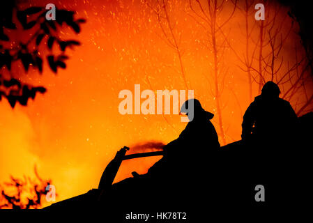 Silhouettes of firemen on the roof of a burning house Stock Photo