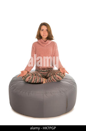 Woman meditates while sitting in the lotus position on round shape grey beanbag chair isolated on white background Stock Photo