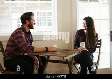 A young man and woman sitting  at a table holding paper cups. Stock Photo
