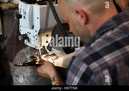 A man using an industriall sewing machine, stitching leather handmade goods. Stock Photo