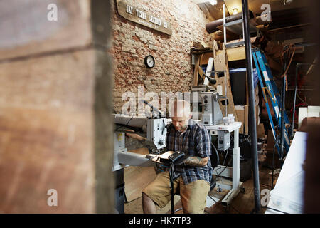 A leather worker, craftsman using an industrial sewing machine on leather material ion his workshop. Stock Photo