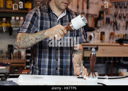 A man working at a bench in a leather workshop, using a mallet and chisel to mark leather. Stock Photo