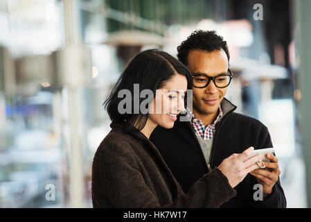 A young man and woman holding a cellphone together and looking at the screen. Stock Photo