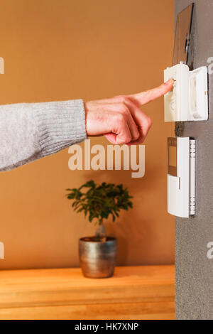 Young male hand pressing button of electronic appliance on wall of modern home. Clean background scene gray wool sweater. Stock Photo