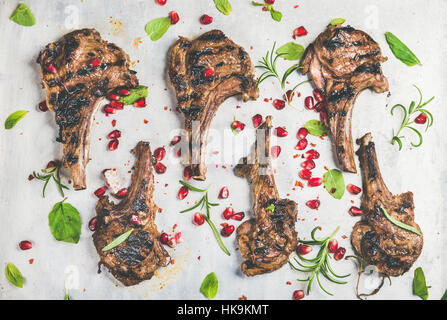 Grilled lamb ribs with pomegranate seeds, fresh mint and rosemary over metal baking tray background, top view, horizontal composition. Meat barbecue a Stock Photo