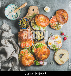 Variety of bagels with smoked salmon, eggs, radish, avocado, cucumber, greens and cream cheese in bowl for breakfast, lunch, party or takeaway on wood Stock Photo