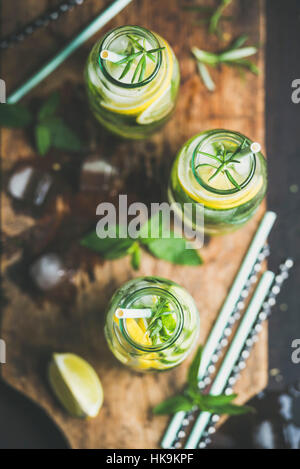 Citrus fruit and herbs infused sassi water for detox, healthy eating, dieting in glass bottles on wooden board over dark background, top view, selecti Stock Photo