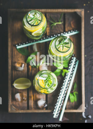 Citrus and herbs infused sassi water for detox, healthy eating, dieting in glass bottles in wooden tray over dark background, selective focus, top vie Stock Photo