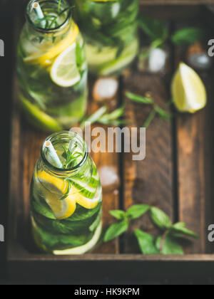 Citrus fruit and herbs infused sassi water for detox, healthy eating, dieting in glass bottles in wooden tray, selective focus, copy space. Clean eati Stock Photo