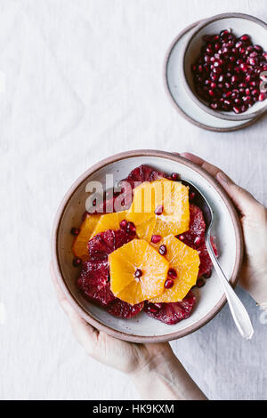 A woman is holding a plate of sliced oranges and pomegranate seeds is photographed from the top view. Stock Photo