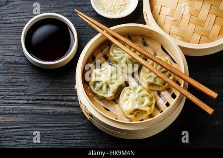 Steamed dumplings Dim Sum in bamboo steamer on black burned wooden background Stock Photo