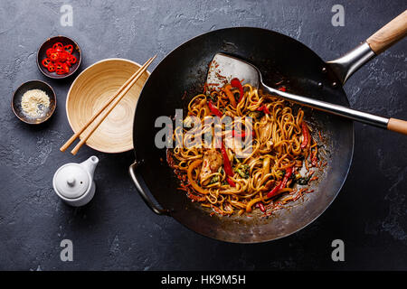 Udon stir-fry noodles with chicken and vegetables in wok pan on dark stone background Stock Photo