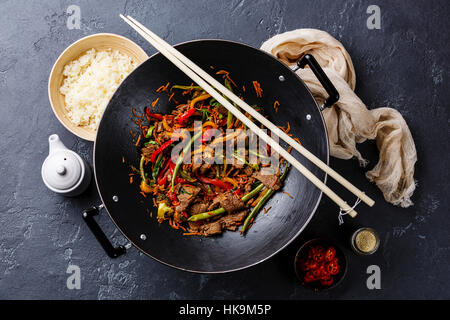 Stir fry beef meat with vegetables and rice in wok pan on dark stone background Stock Photo