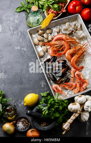 Raw fresh Seafood Cocktail with Clams and Shrimps and Ingredients for cooking pasta Spaghetti on concrete background