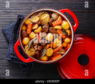 Beef meat stewed with potatoes, carrots and spices in cast iron pot on burned black wooden background Stock Photo