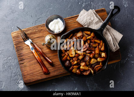 Fried potatoes roasted with porcini wild mushrooms in black iron pan on dark stone background Stock Photo