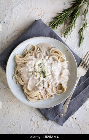 Rosemary Gorgonzola Pesto Cream Sauce over Spaghetti.  Photographed from top view on a white/yellow/peach colored plaster background. Stock Photo
