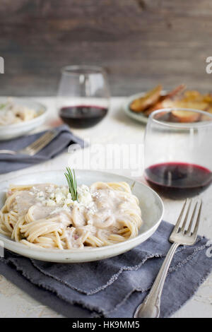 Rosemary Gorgonzola Pesto Cream Sauce over Spaghetti served with red wine and crostini.  Photographed from front view on a white/yellow/peach colored Stock Photo