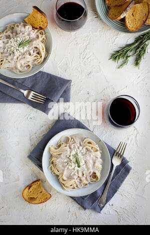 Rosemary Gorgonzola Pesto Cream Sauce over Spaghetti served with red wine and crostini.  Photographed from top view on a white/yellow/peach colored pl Stock Photo