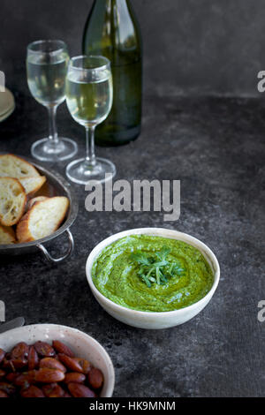 Arugula Chive Basil Pesto served in a ceramic bowl with crostini, almonds and wine.  Photographed fron front view on a black/brown background. Stock Photo