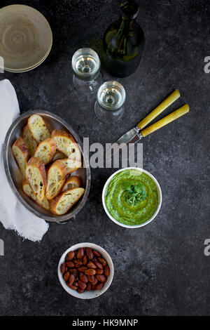 Arugula Chive Basil Pesto served in a ceramic bowl with crostini, almonds and wine. Stock Photo