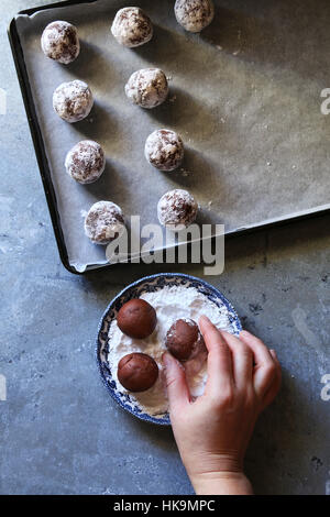 Making chocolate crinkle cookies.Female hand coating dough ball with icing sugar.Top view Stock Photo