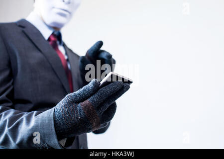 Business man in white mask wearing gloves and using mobile phone - fraud, hacker, theft, cyber crime concept Stock Photo