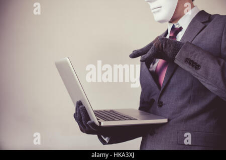 Business man in white mask wearing gloves and using computer - fraud, hacker, theft, cyber crime concept Stock Photo