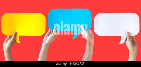 Human Hands Holding Yellow, Blue and White Speech Bubbles Over Light Orange Red Background - Fun Balloon speech bubble concept Stock Photo