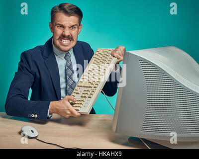 Angry businessman breaking keyboard against blue background Stock Photo