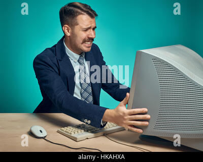 Angry businessman using a monitor against blue background Stock Photo