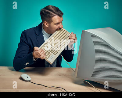 Angry businessman breaking keyboard against blue background Stock Photo