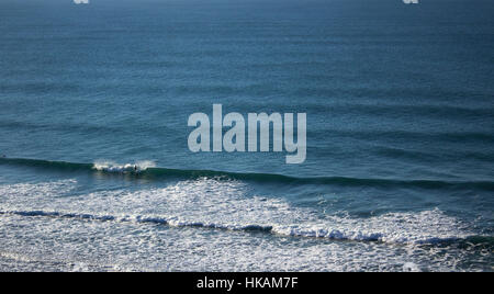 A surfer rides waves in an empty lineup at a beach called Chapel Porth, situated on the Cornish Coast. Stock Photo