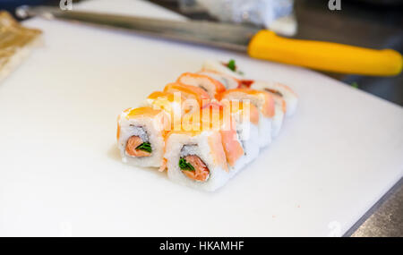 Traditional Japanese sushi rolls with salmon lay on white cutting board with chief knife. Closeup photo with selective focus Stock Photo