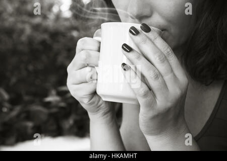 Young woman drinks coffee from white cup. Close-up black and white photo, selective focus on hands Stock Photo