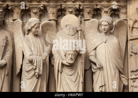 Saint Denis (Dionysius) holding his head and surrounded by angels. Neo-Gothic statue on the main facade of the Notre-Dame Cathedral (Notre-Dame de Paris) in Paris, France. Damaged Gothic statues on the main facade were restored by French architects Eugene Viollet-le-Duc and Jean-Baptiste Lassus in the 1840s. Stock Photo