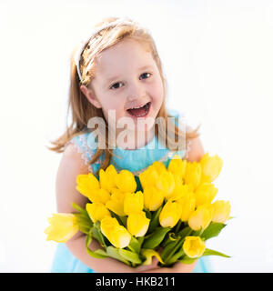 Cute little girl in blue dress holding tulip flowers bouquet on birthday party. Spring and Easter decoration. Stock Photo