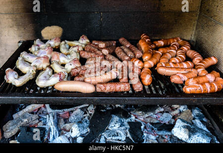 Mixed variety of Meat on barbecue grill with coal. Cevapcici, sausages, chicken wings and hot dogs on charcoal barbecue BBQ. Stock Photo
