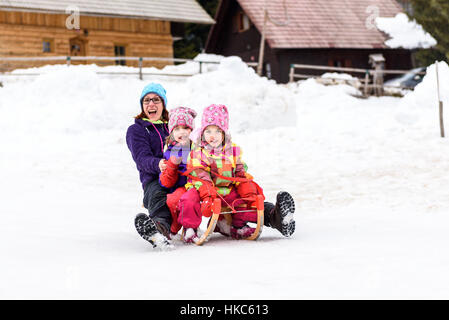 Family is sledding down the snowy slope. Family enjoying active vacation on ski sledge. Stock Photo