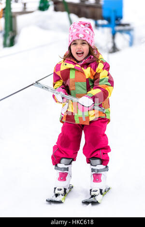 Little girl is learning to ski in ski resort. Child is using ski baby lift conveyor skiing for the first time. Active children are happy. Stock Photo