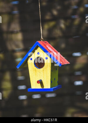 An old weathered DIY birdhouse hanging from the tree. Colorful small bird house with red roof, yellow walls and blue spots. Stock Photo