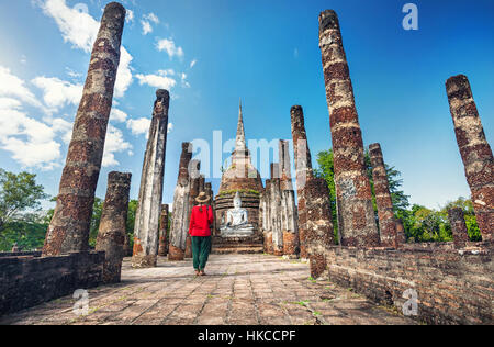 Tourist Woman in red costume looking at ancient Buddha statue in Wat Sa Si of Sukhothai Historical Park, Thailand