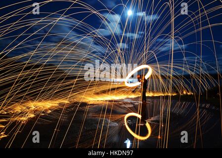 A long exposure of steel wool spinning on a with sparks reflected in a lake Stock Photo