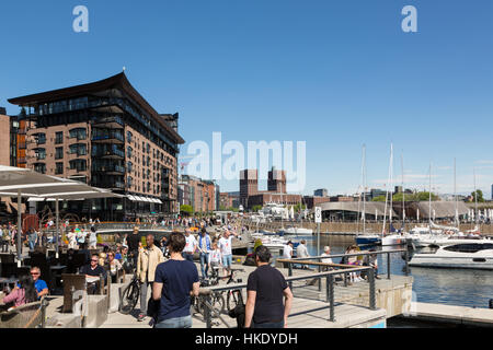 OSLO - MAY 16, 2016: People enjoy lunch in restaurants along the renovated Aker Brygge harbor on a sunny day in Norway capital city. The building in t Stock Photo