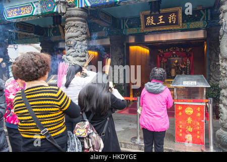 faithful in prayer while offering incense sticks  in  Sik Sik Yuen Wong Tai Sin temple in Hong Kong Stock Photo